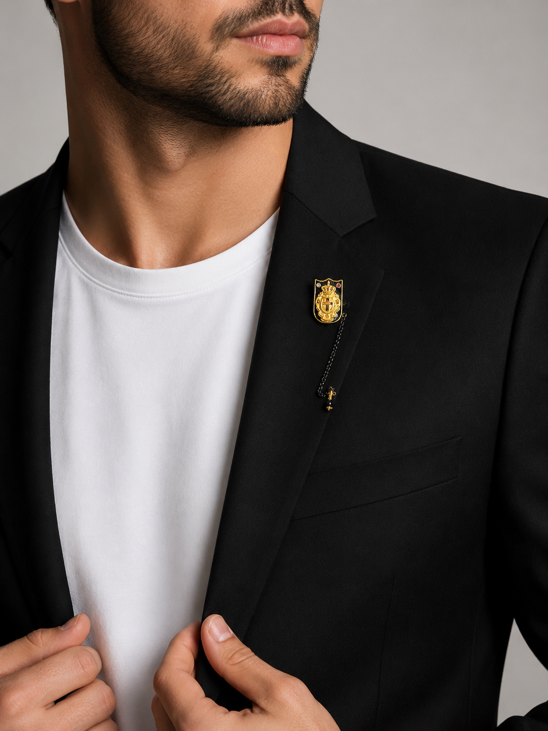 Man wearing a black blazer with a gold pin on a gray background