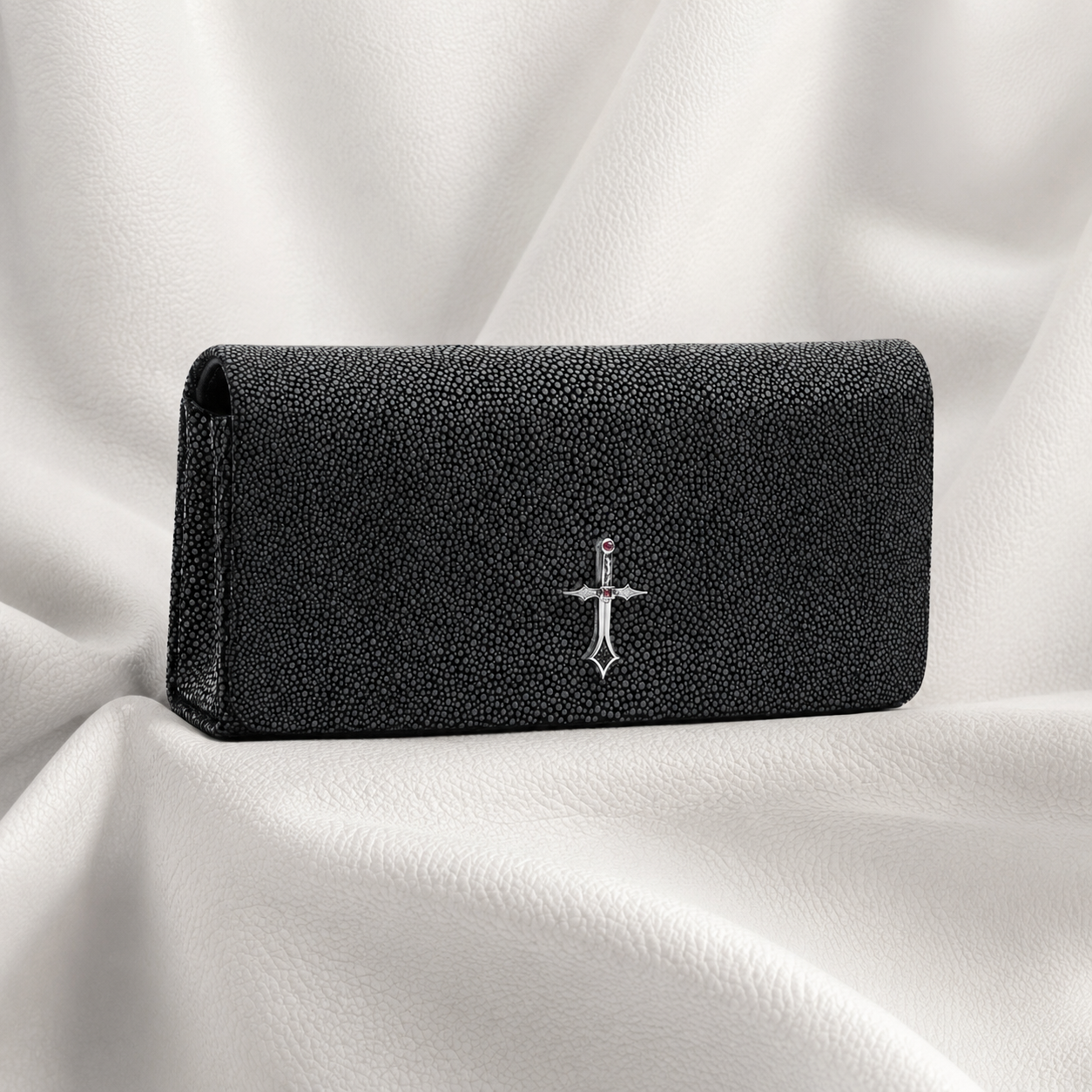 Black textured wallet with a silver emblem on a white fabric background