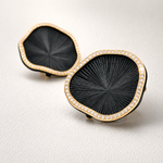 Pair of black earrings with gold accents on a light gray background